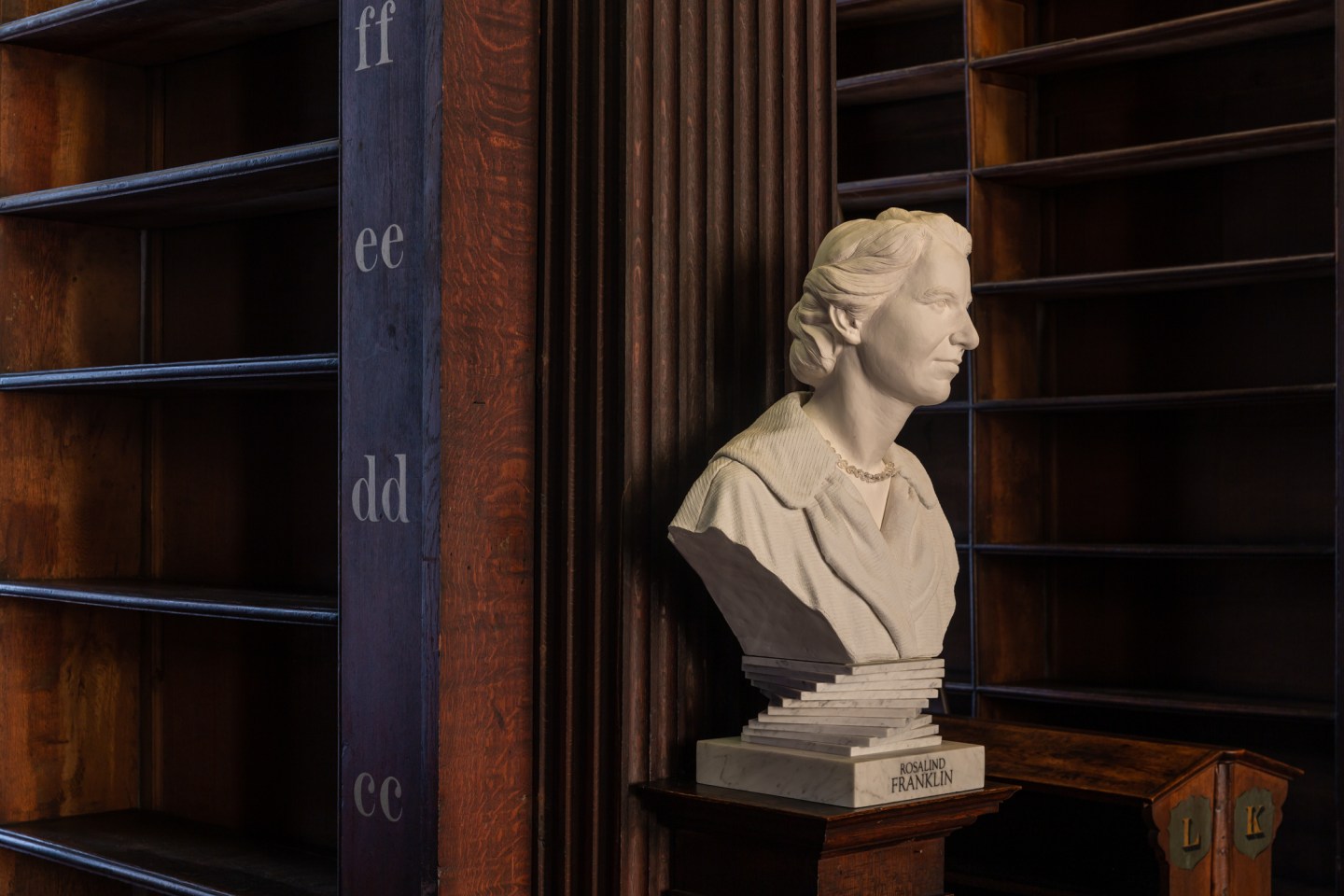 A statue of a woman alongside empty shelves in the Long Room