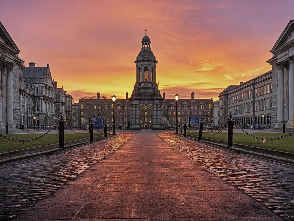 A picture of Trinity College campus with a sunrise backdrop of purple, pink, orange and yellow