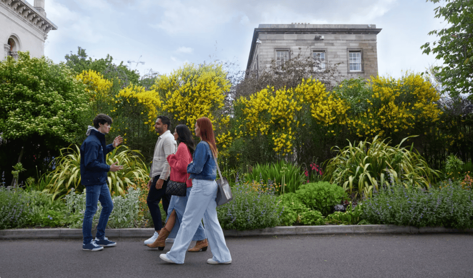 A guide walks near blossoming flowers on Trinity campus with a group of 3 people.